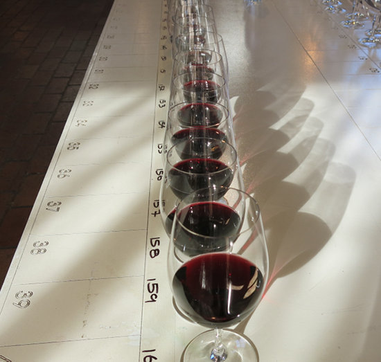 A row of wine glasses with dark red wine, along a very long table with score cards.
